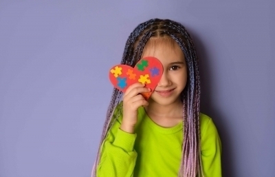 Menina autista sorridente com coração formado por peças coloridas cobrindo parte do rosto